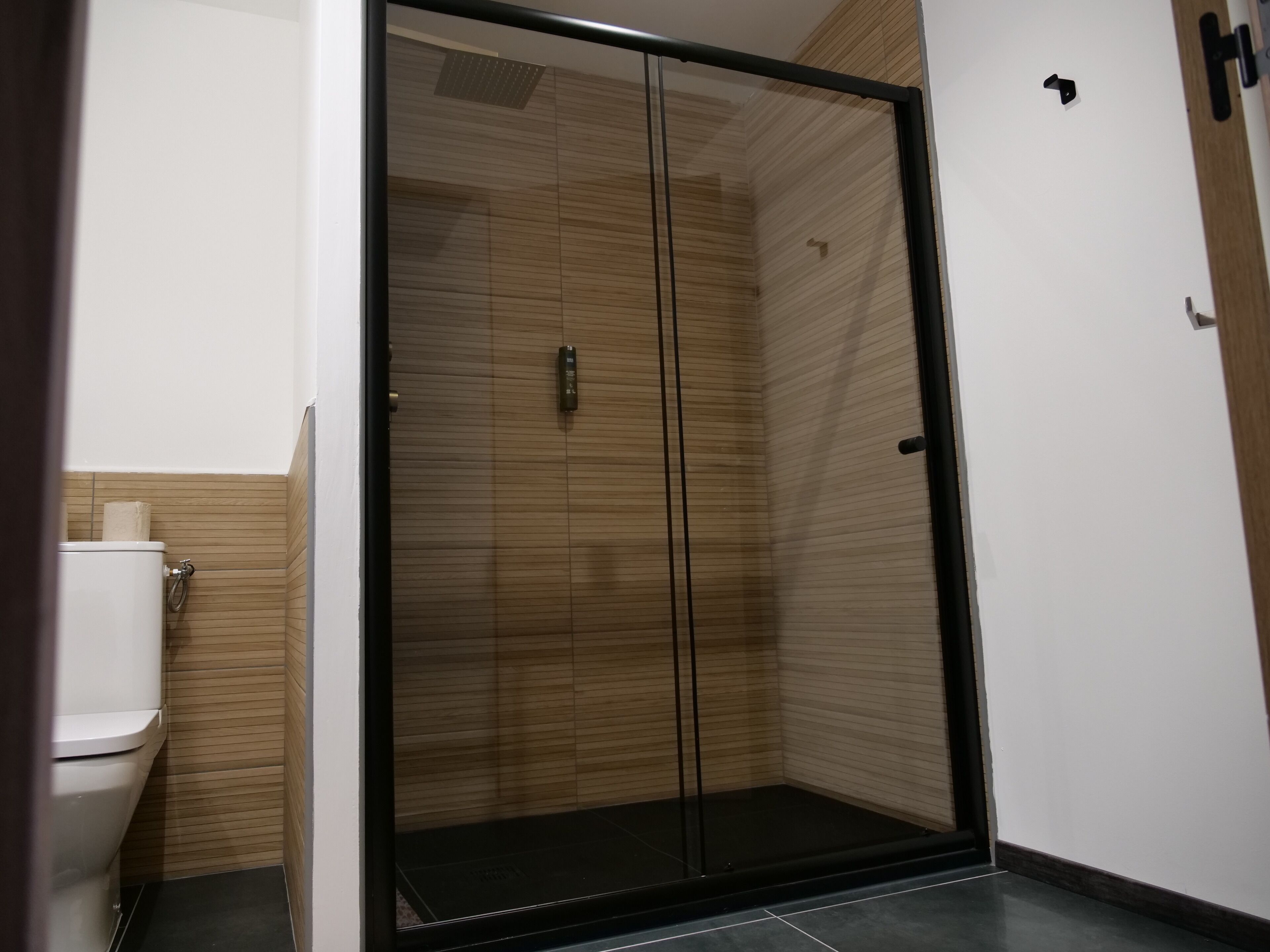 A modern bathroom with a glass shower enclosure, a toilet, and a wooden wall panel.