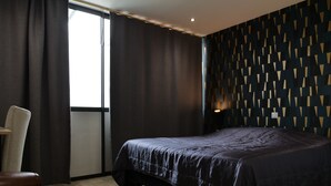 Un dormitorio con una cama grande, una silla, un ventanal y una pared con diseño.