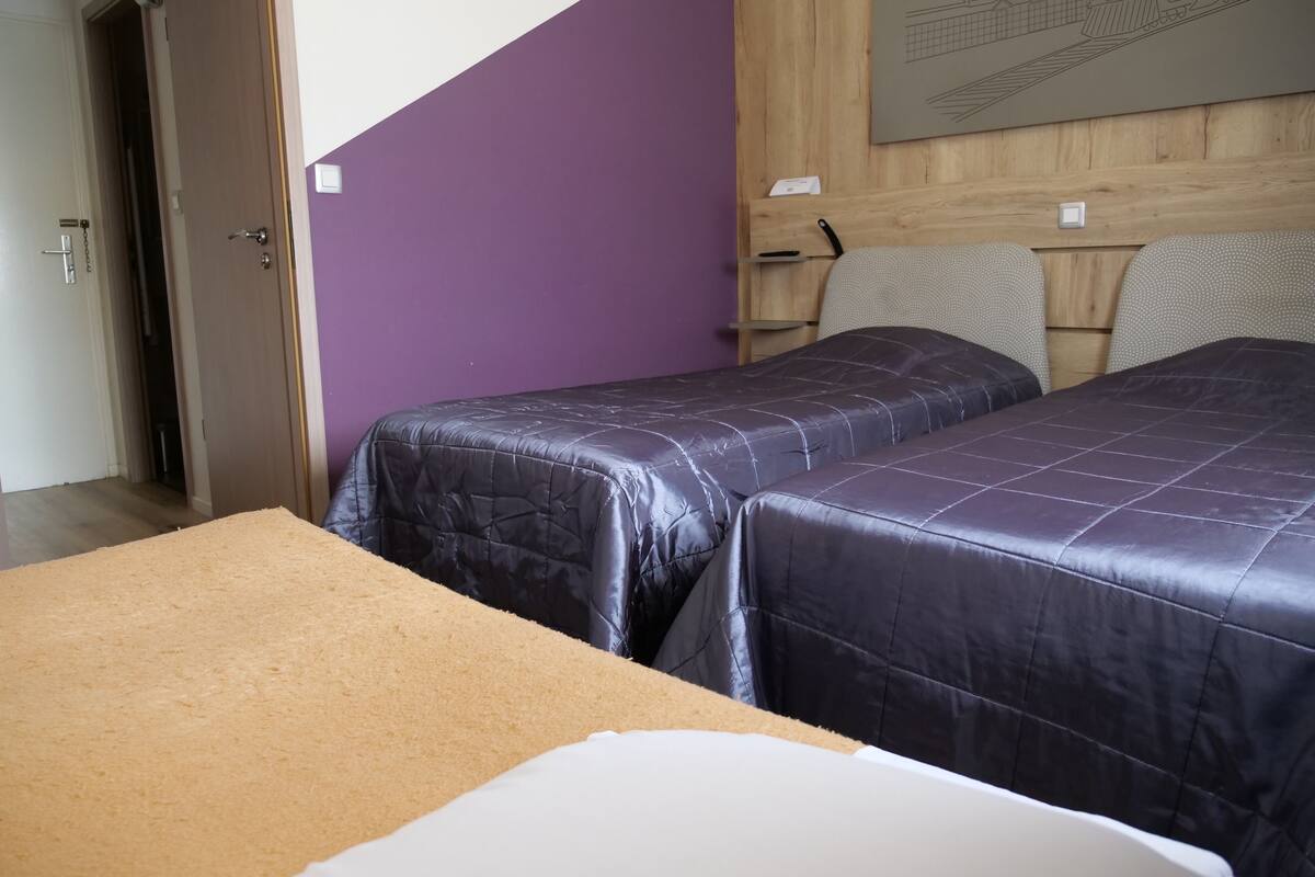 Una habitación con dos camas, cabecero de madera y pared morada.