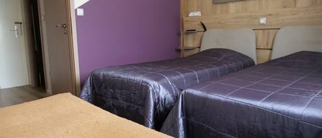 A room with two beds, a wooden headboard, and a purple wall.