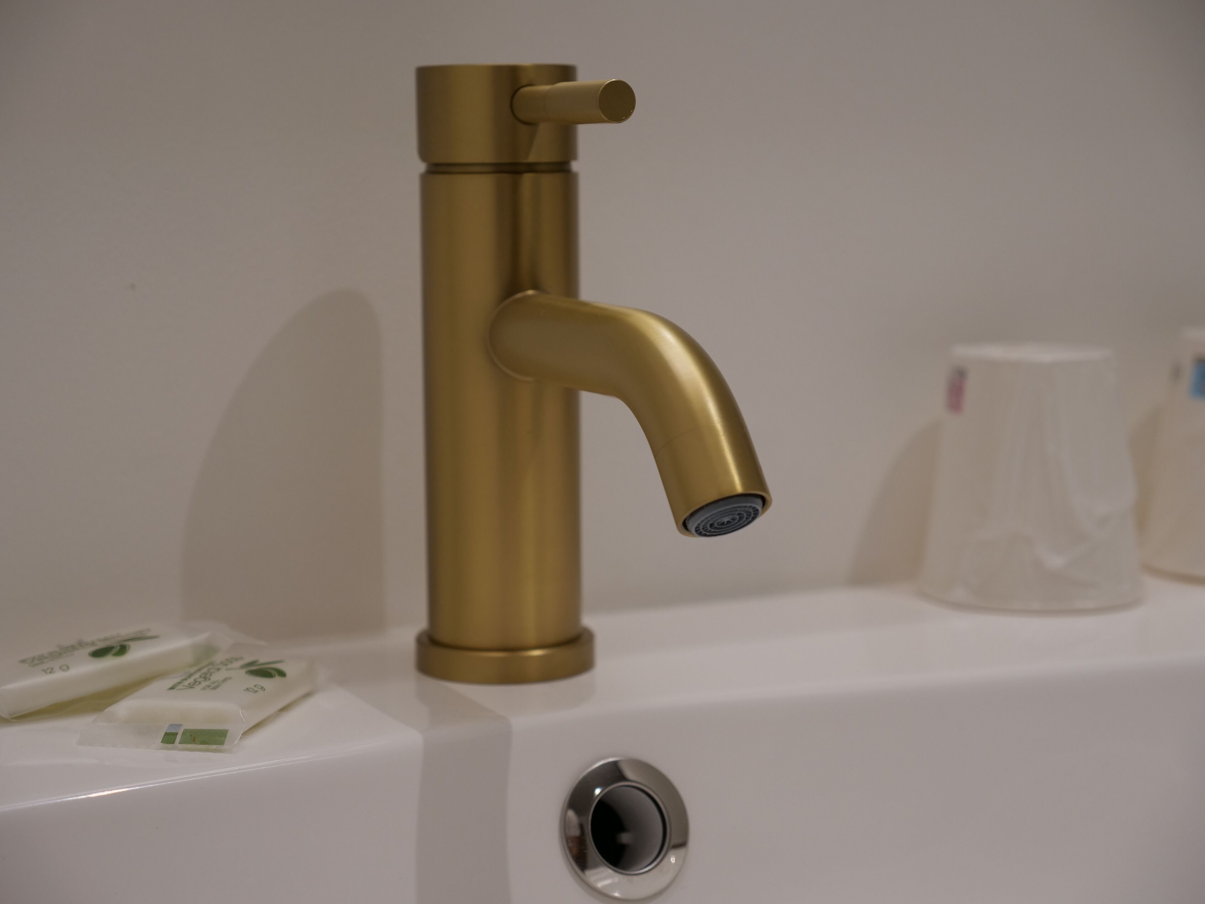 A bathroom with a gold faucet, a sink, and two bottles of liquid soap.
