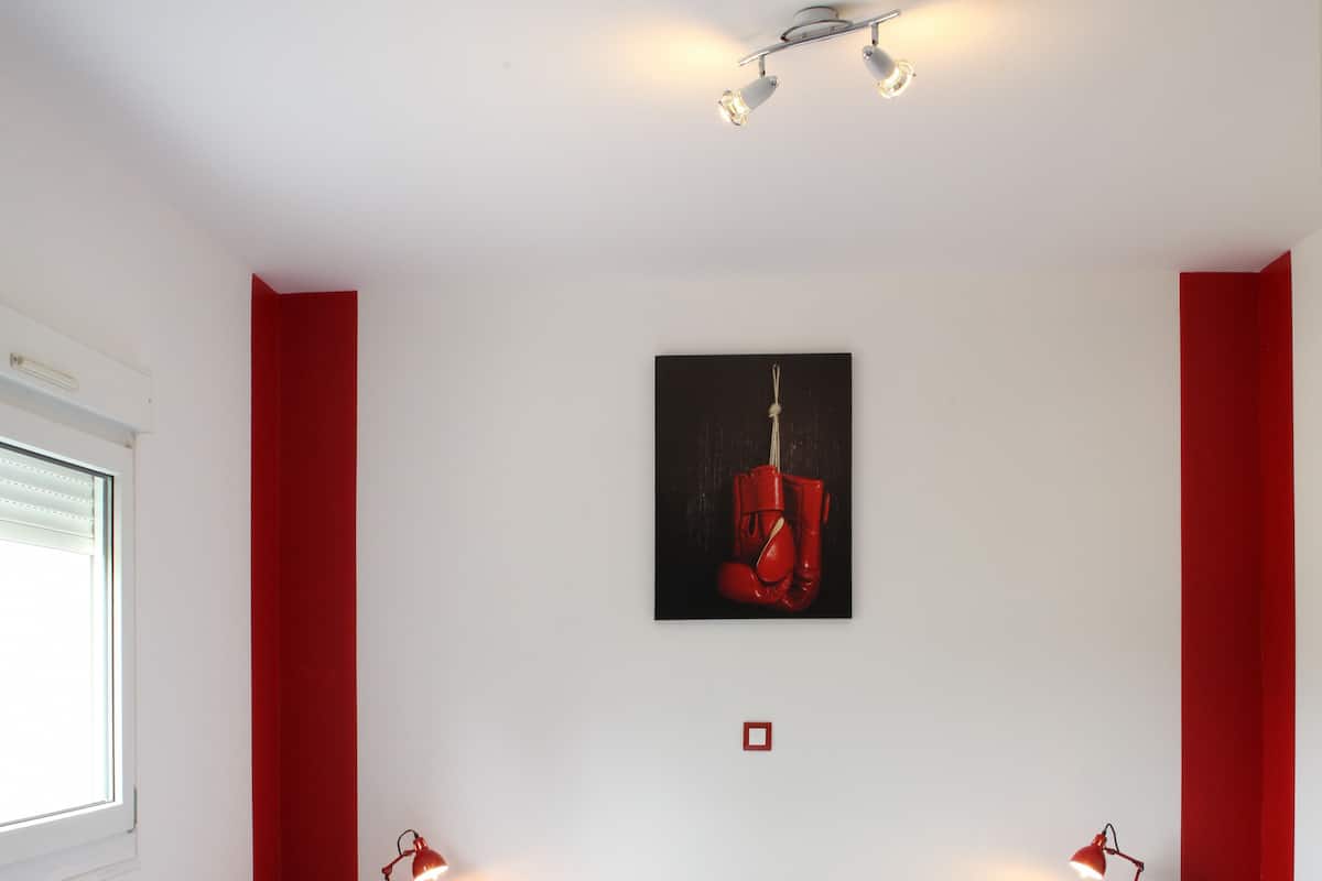 Un dormitorio con una cama, dos mesitas de noche con lámparas, una ventana y un cuadro en la pared.