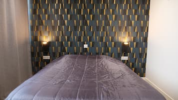 Ein Zimmer mit Wandverkleidung, einem Bett mit dunkel gestreifter Bettdecke, zwei Wandlampen und einer Klimaanlage.