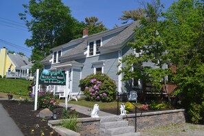 A bed and breakfast named 'Moon Over Maine' with a stone staircase leading to the entrance, surrounded by lush greenery and a well-maintained garden.