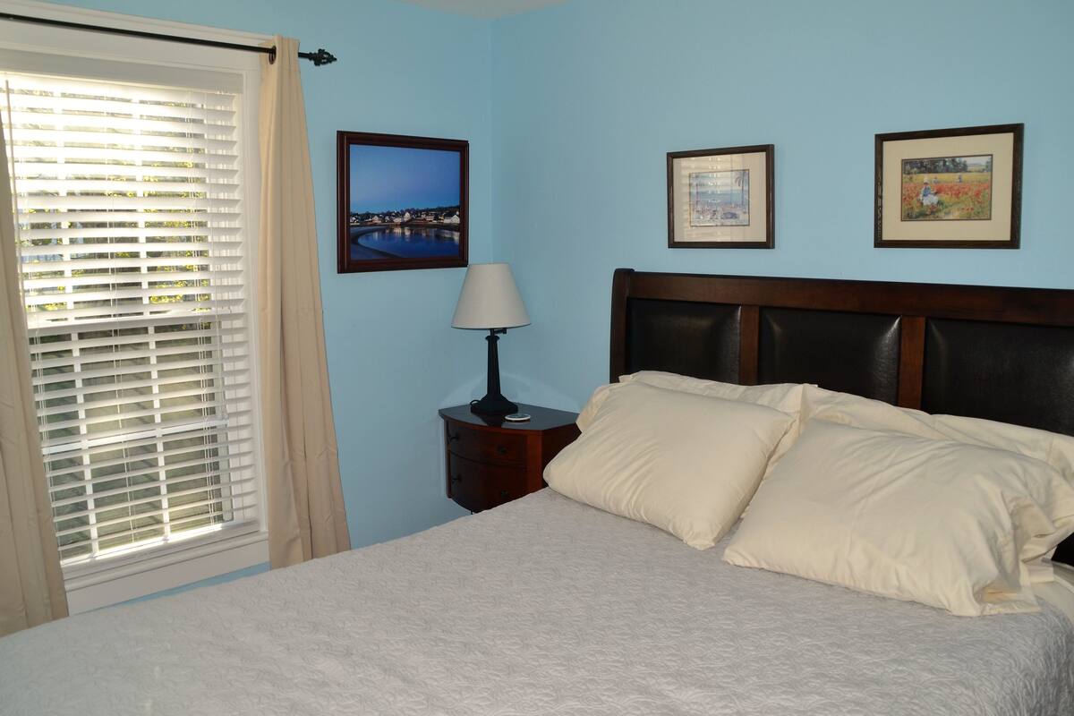 A bedroom with a bed, a nightstand with a lamp, and three framed pictures on the wall.