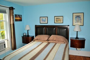 A bedroom with a bed, two nightstands, a window with curtains, and three framed pictures on the wall.