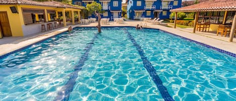 Una piscina con agua azul cristalina, rodeada de edificios con tejados de cerámica y zonas de estar al aire libre.
