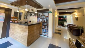 A modern hotel lobby with a reception desk, a tips box, a bookshelf, and a seating area with sofas and a coffee table. - Lemon Tree Hotel (Kathmandu)