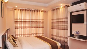 A hotel room with a bed, curtains, a mounted TV, and a small shelf with bottles. - Lemon Tree Hotel (Kathmandu)