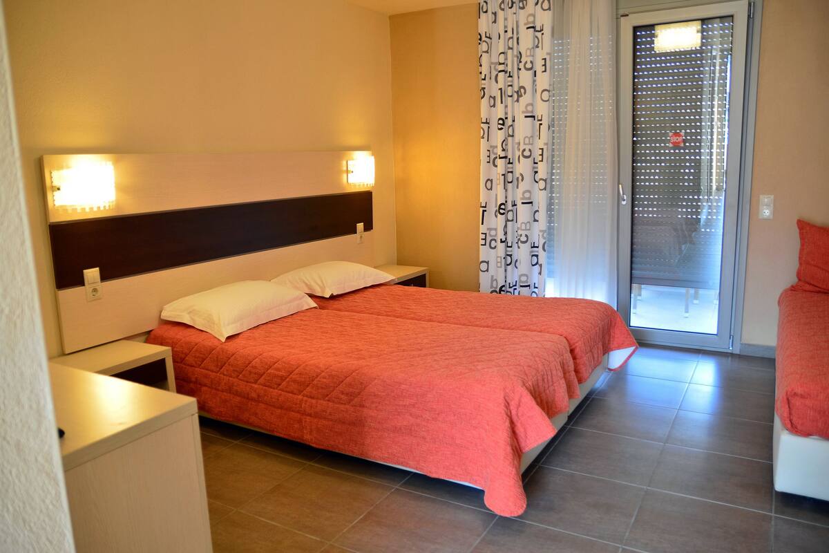 Habitación de hotel con cama, mesitas de noche, ventana con cortina y puerta.
