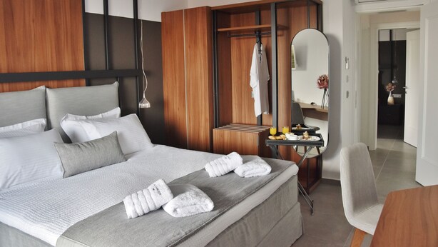 Una habitación de hotel moderna con una cama grande, un armario de madera, un escritorio pequeño con espejo y una silla.