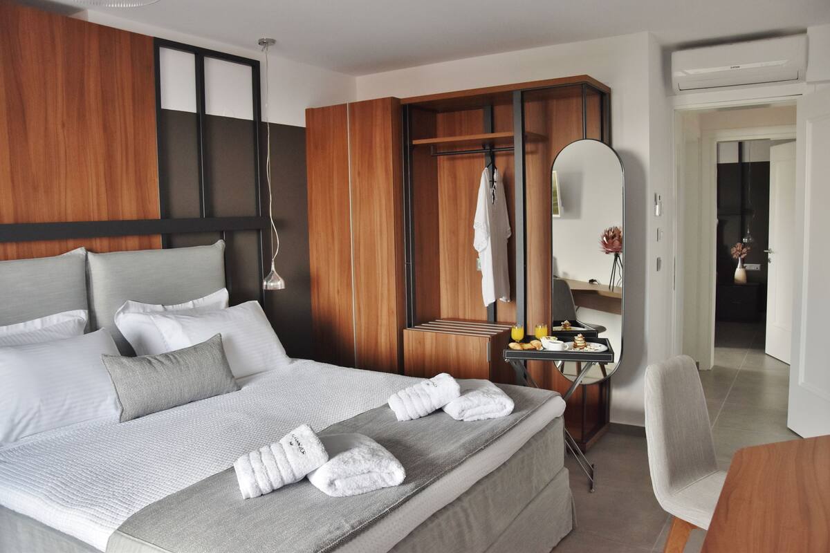 Una habitación de hotel moderna con una cama grande, un armario de madera, un escritorio pequeño con espejo y una silla.