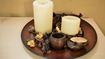 Two candles on a wooden plate with dried flowers and a small bowl.