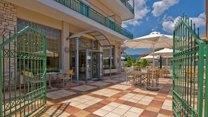 Un patio de hotel con mobiliario exterior, una entrada de vidrio y vistas a la montaña.