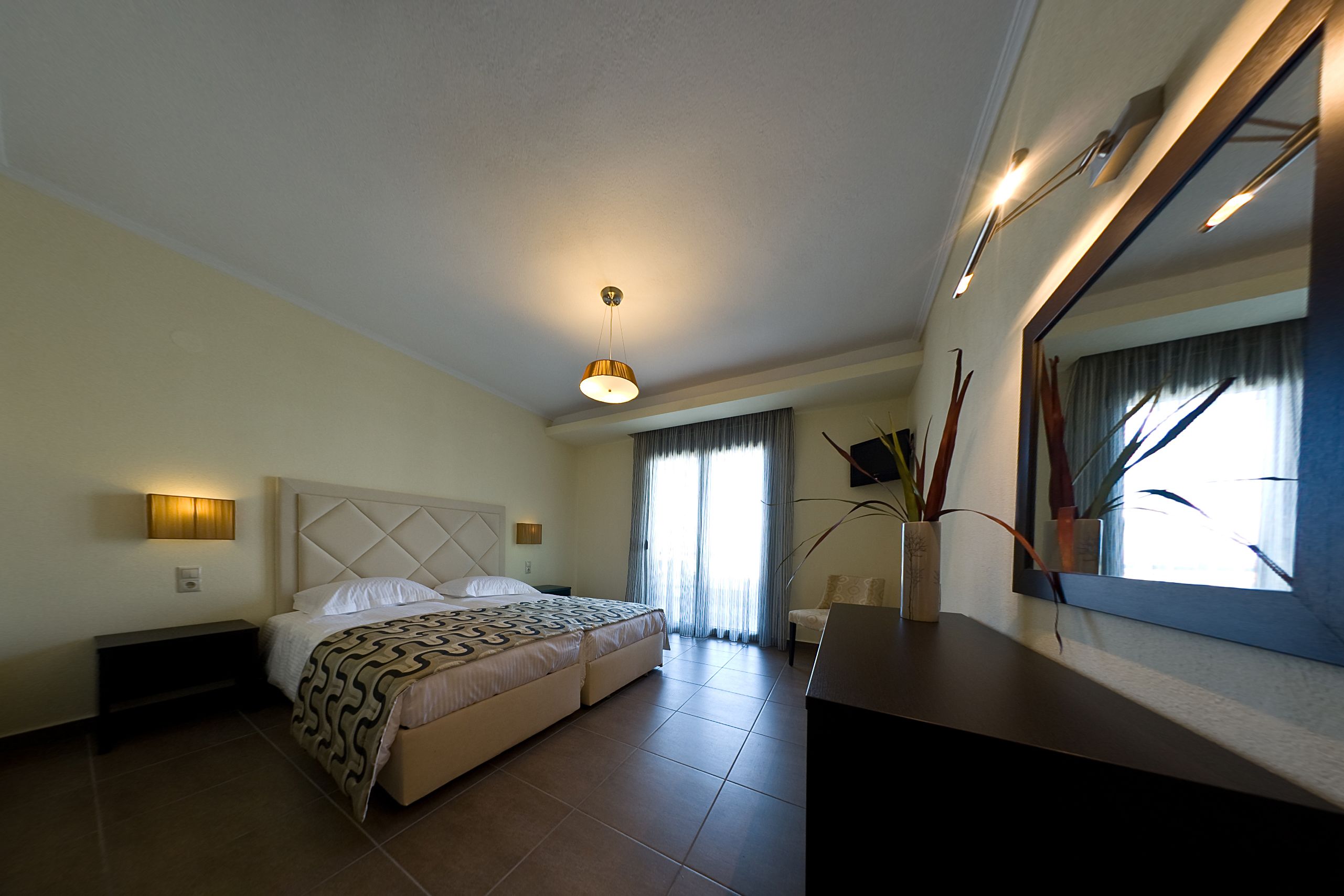 Una habitación de hotel con cama, mesita de noche, lámpara y un espejo grande.
