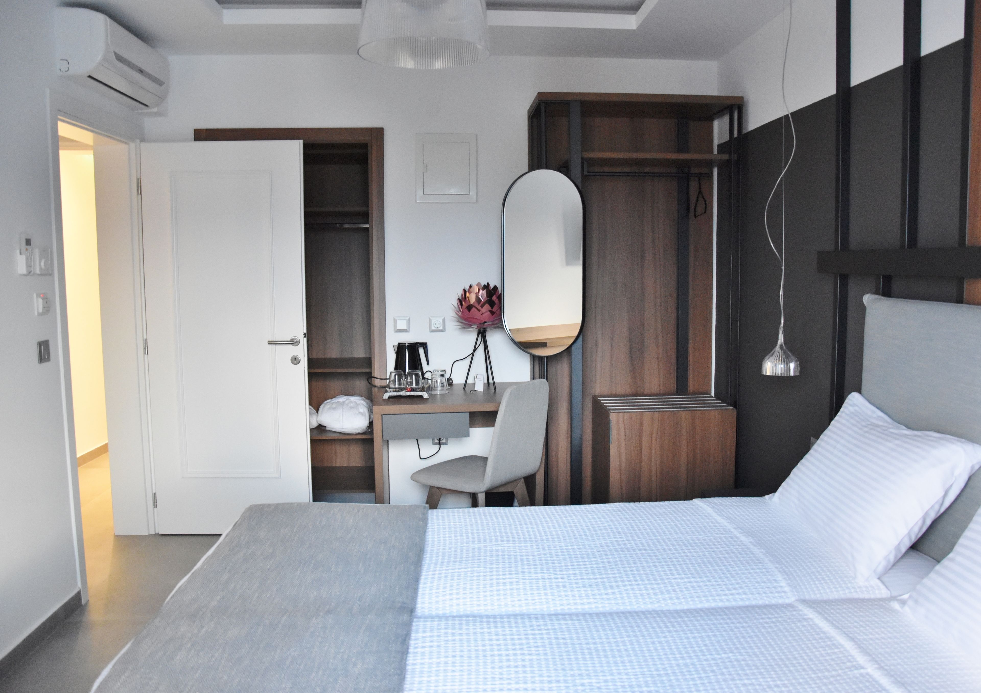 Ein modernes Hotelzimmer mit einem großen Bett, einem Schreibtisch mit Stuhl, einem Spiegel und einem Kleiderschrank.