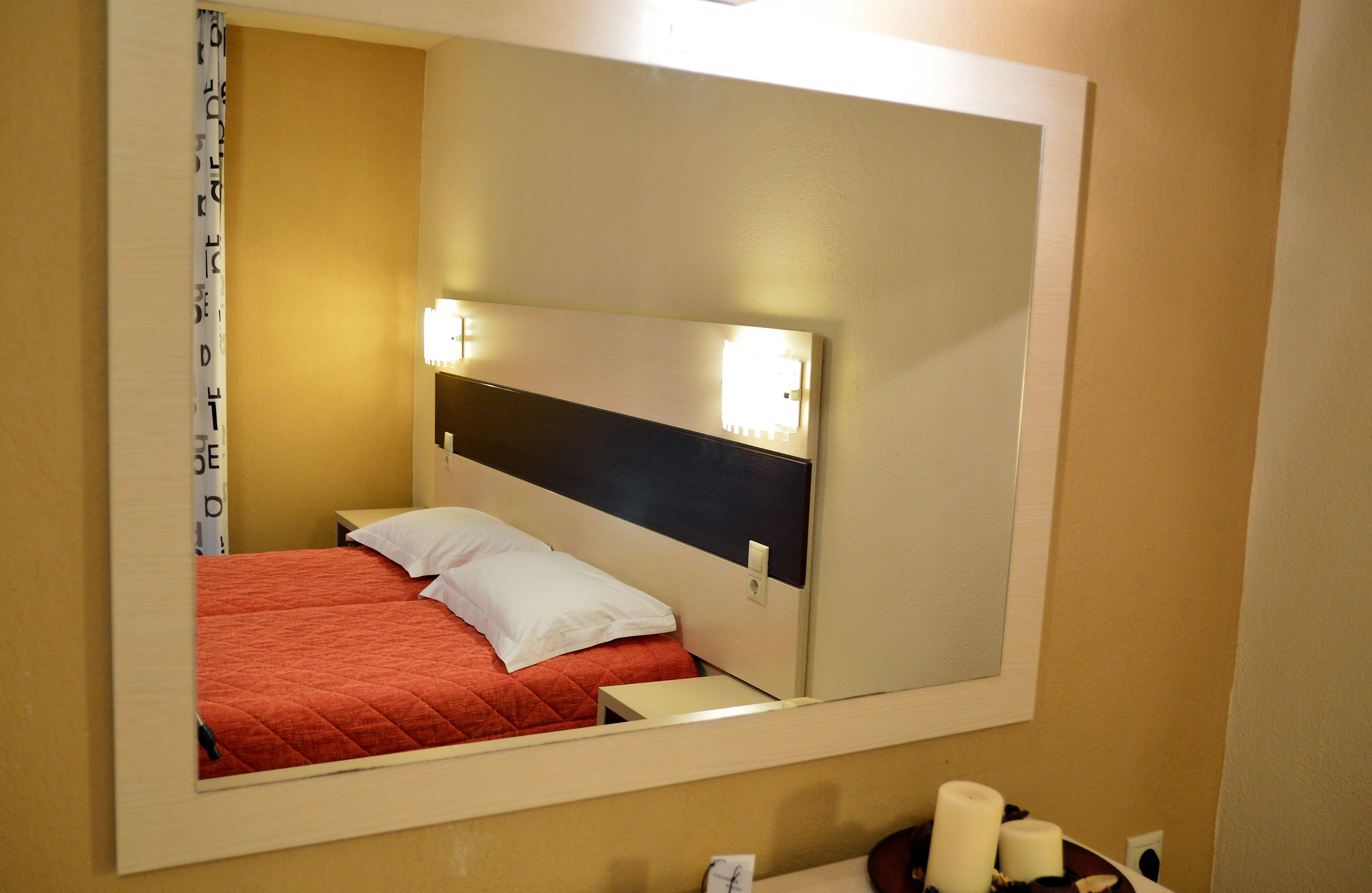 A hotel room with a bed, a nightstand, a mirror, and a wall-mounted light fixture.