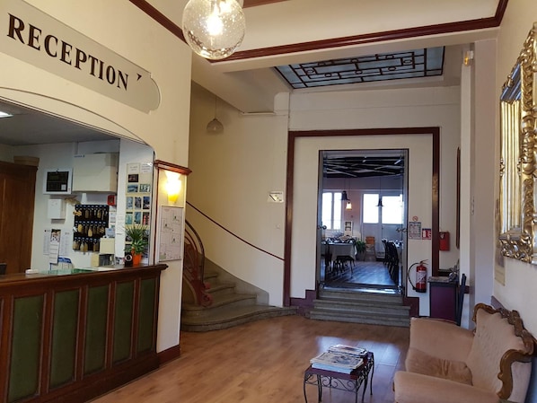 A reception area with a counter, a staircase, and a dining area in the background.