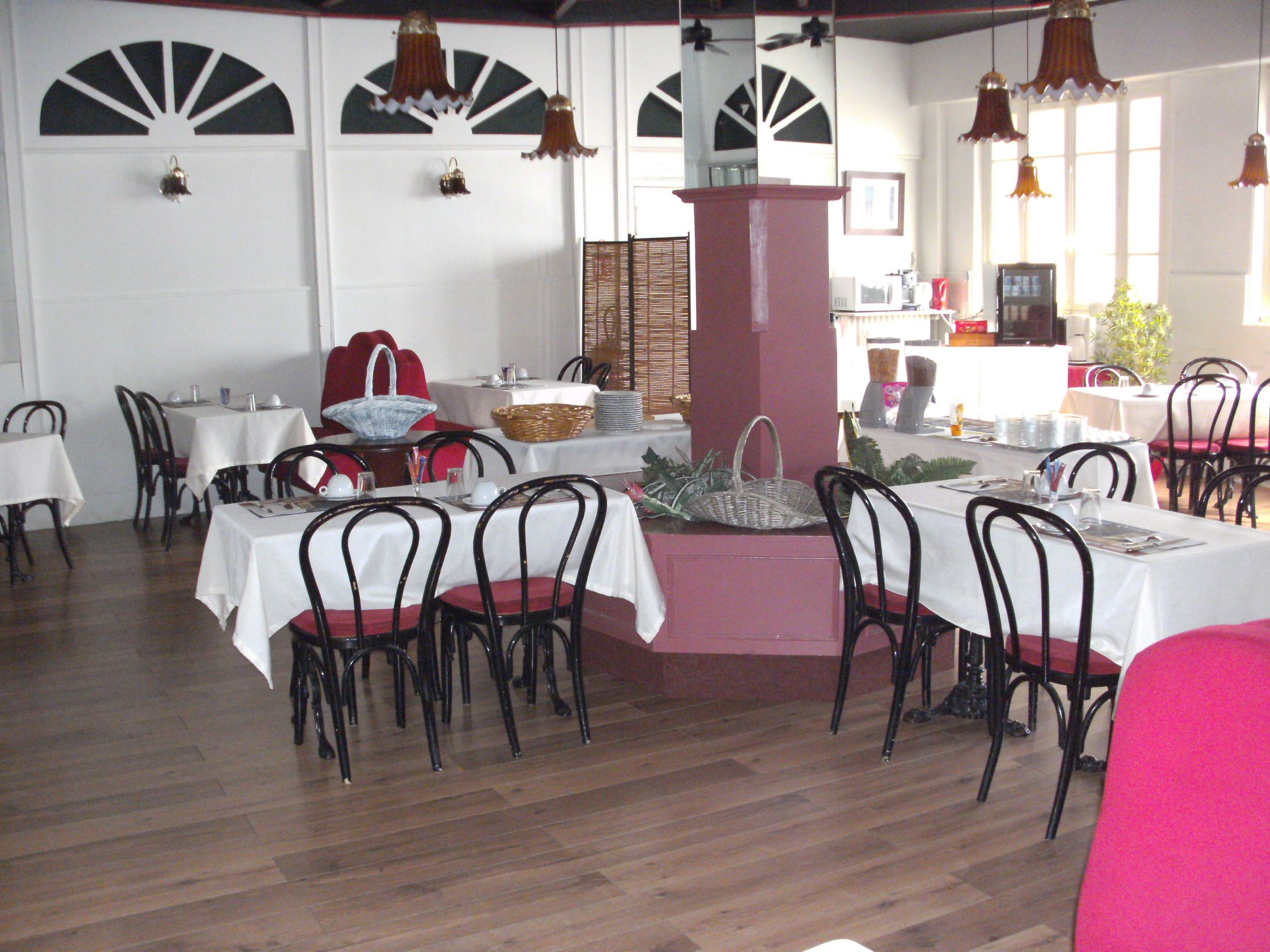 Un restaurant doté de nombreuses tables et chaises, de nappes blanches et de luminaires suspendus.