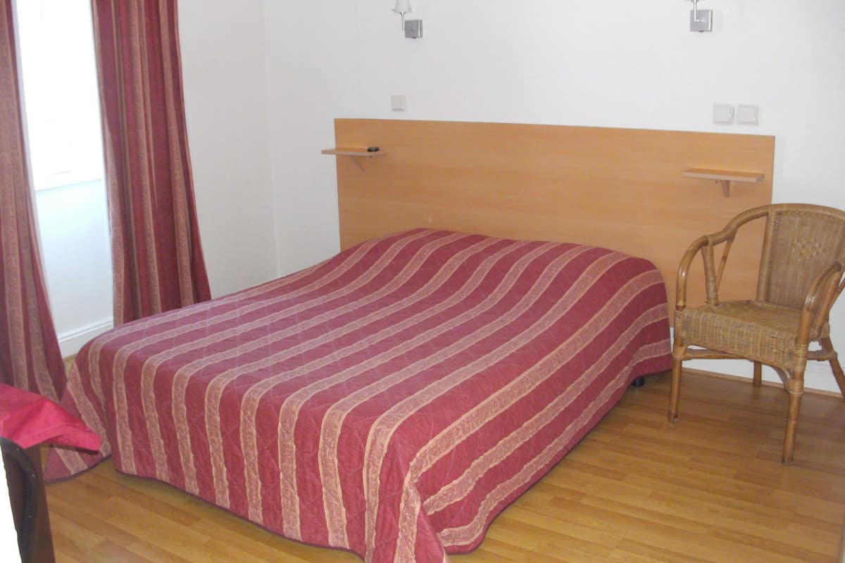 A bedroom with a wooden headboard, a striped bedspread, a wicker chair, and two wall-mounted lamps.