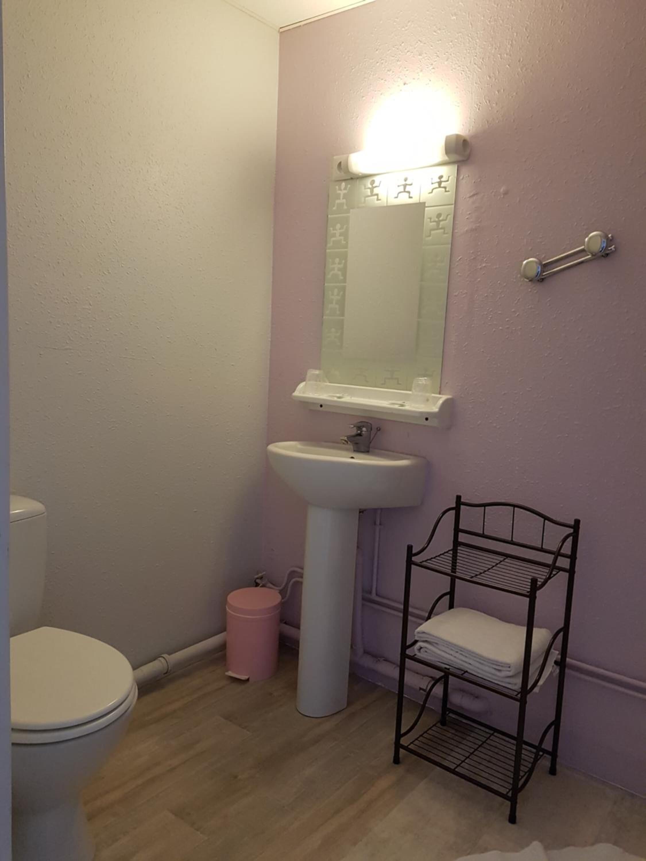 Een badkamer met een wit wastafel, een spiegel, een toilet en een metalen rek met opgevouwen handdoeken.