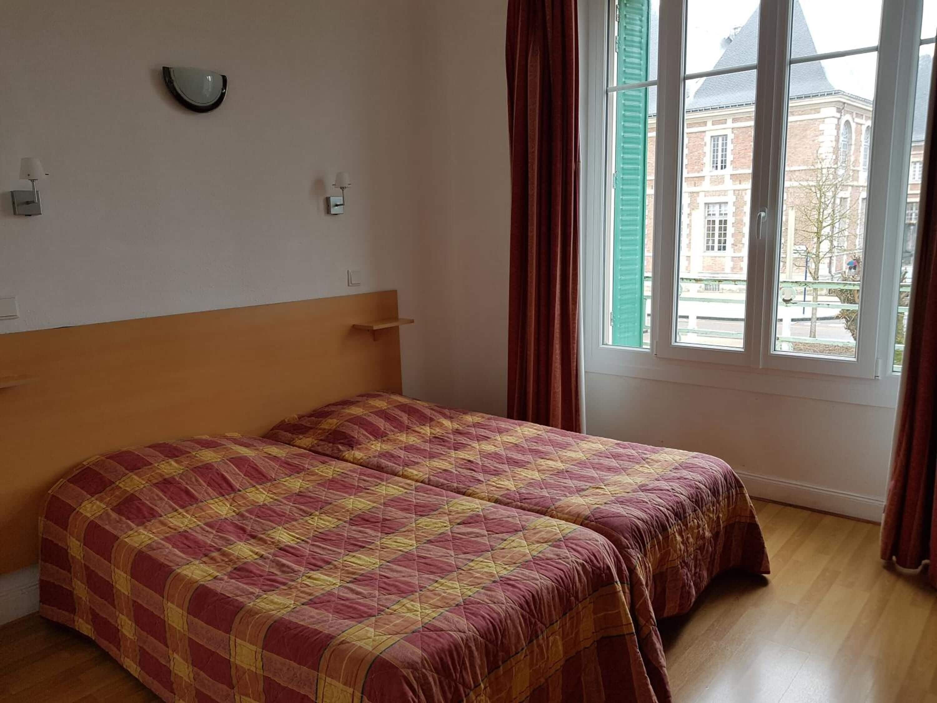 Une pièce avec un lit, une fenêtre avec des rideaux et une vue sur un bâtiment à l’extérieur.
