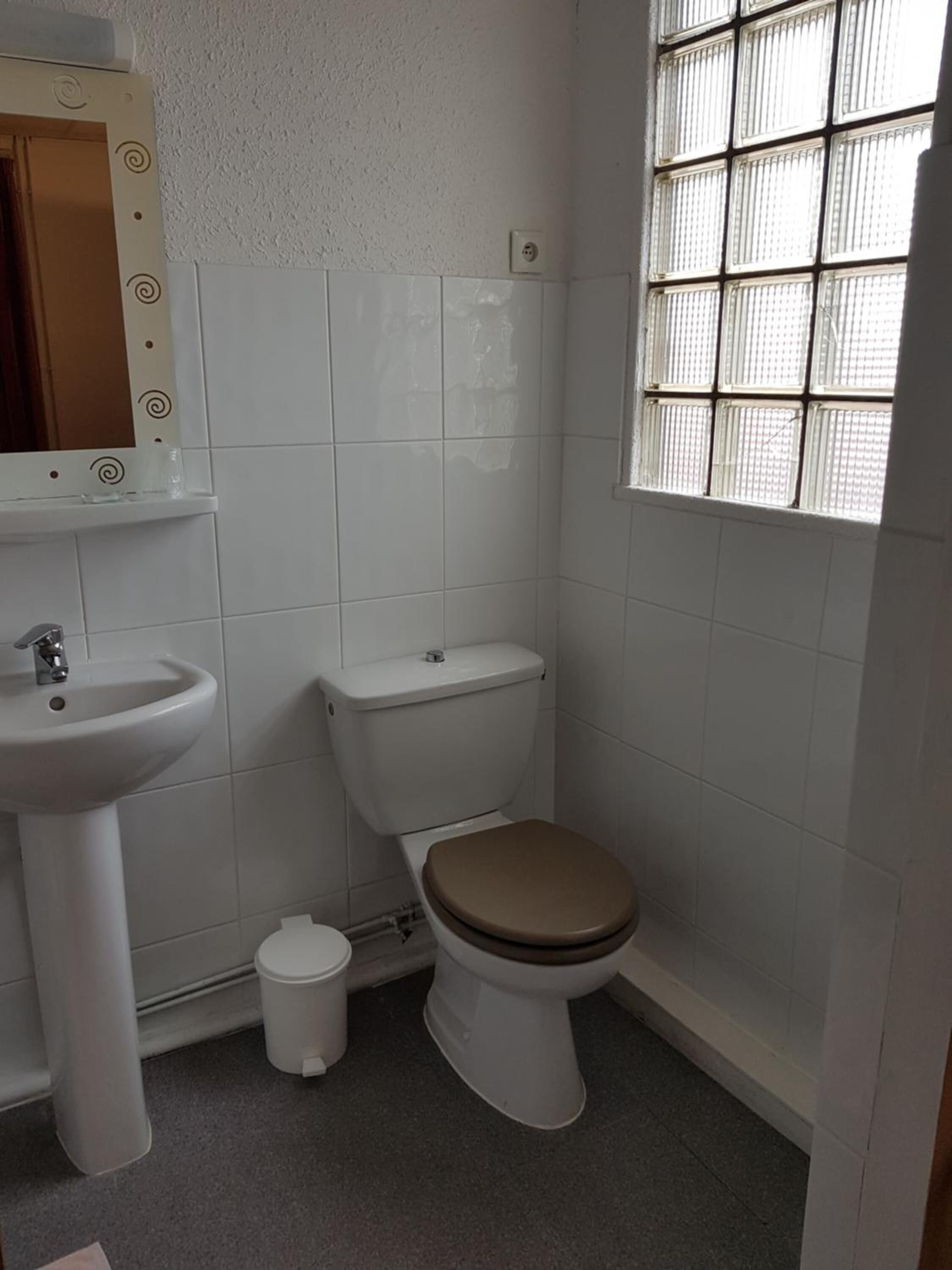 A small bathroom with a toilet, sink, and a window with bars.