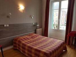 Habitación de hotel con cama, radiador, ventana con cortinas y vistas a edificios.