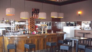 Zona de bar con mostrador de madera, varios taburetes, lámparas colgantes y una cocina al fondo.