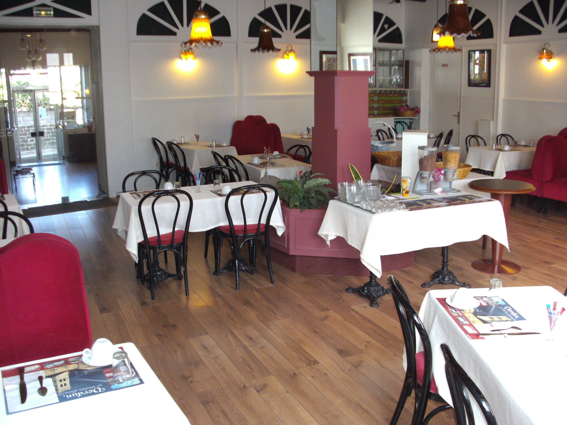 A restaurant with multiple tables and chairs, wooden flooring, and decorative wall sconces.