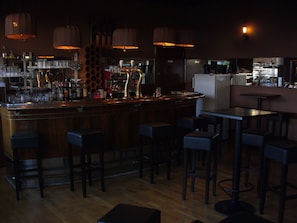 A bar area with a wooden counter, multiple stools, and hanging pendant lights.