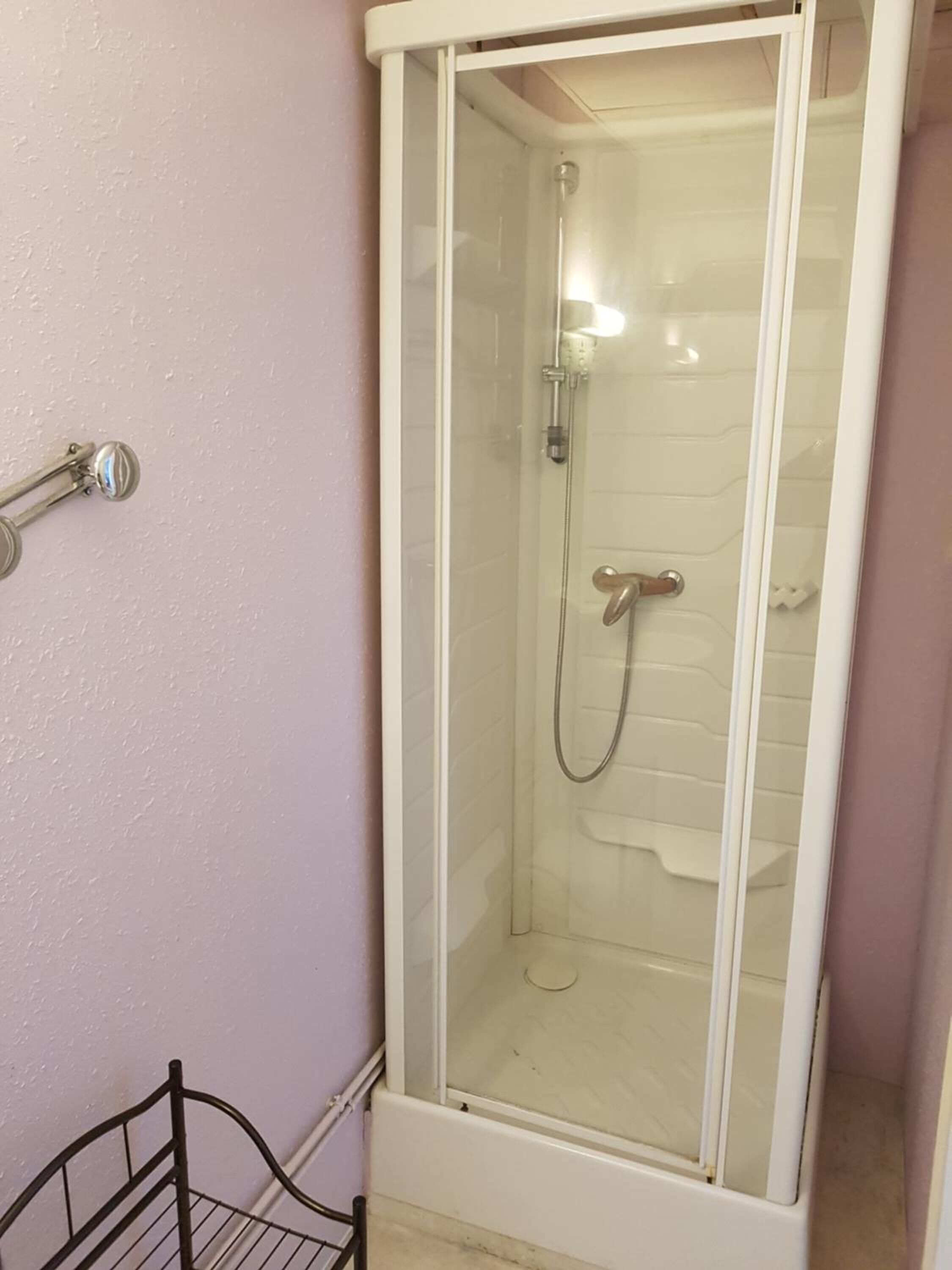 Un espacio de ducha pequeño y cerrado con puerta de vidrio, un cabezal de ducha y un rociador de mano.