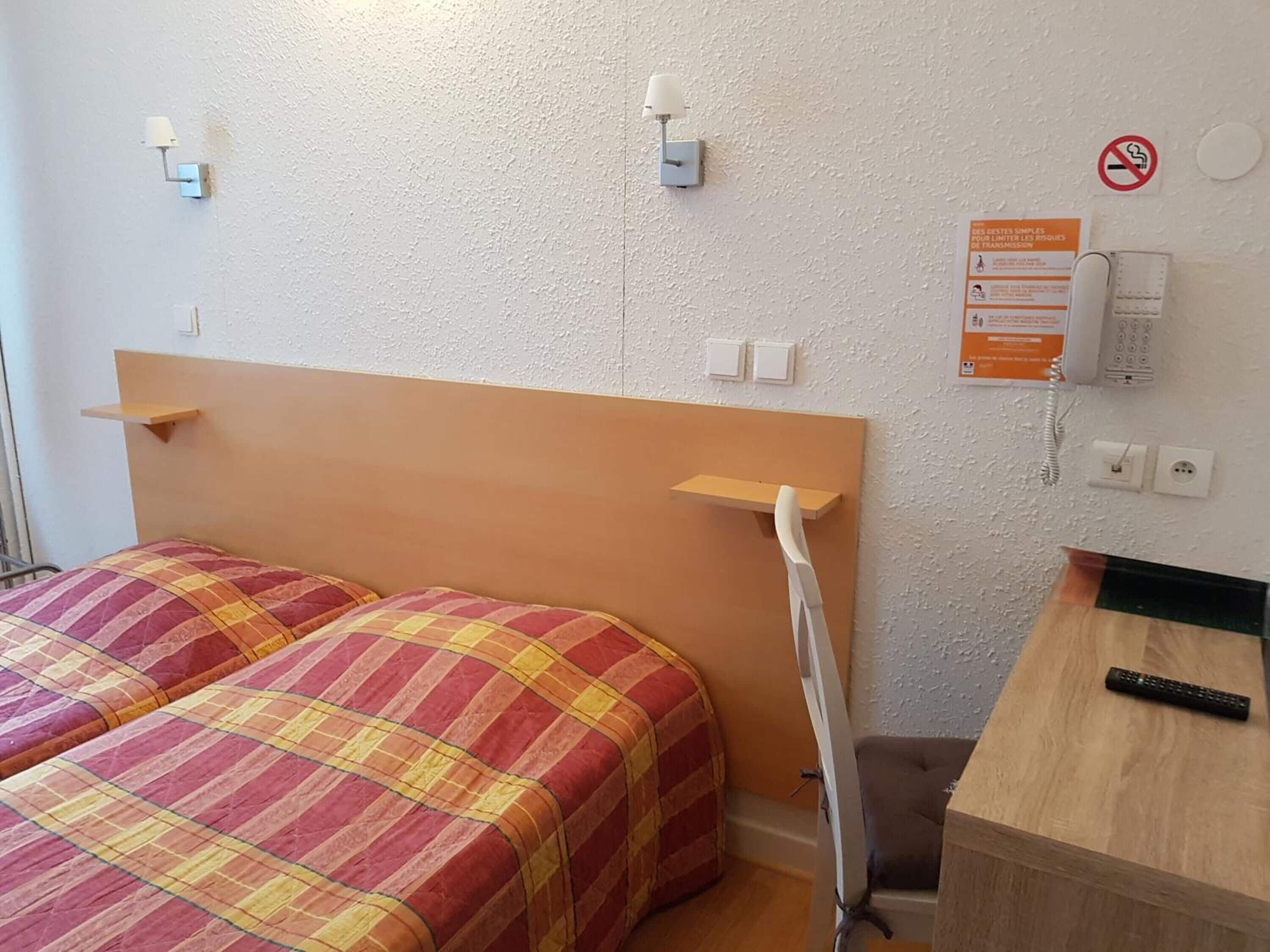 A hotel room with a bed, bedside tables, a desk, a chair, a phone, and a no-smoking sign.