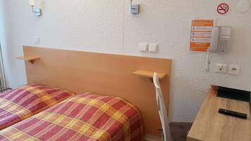 A hotel room with a bed, bedside tables, a desk, a chair, a phone, and a no-smoking sign.