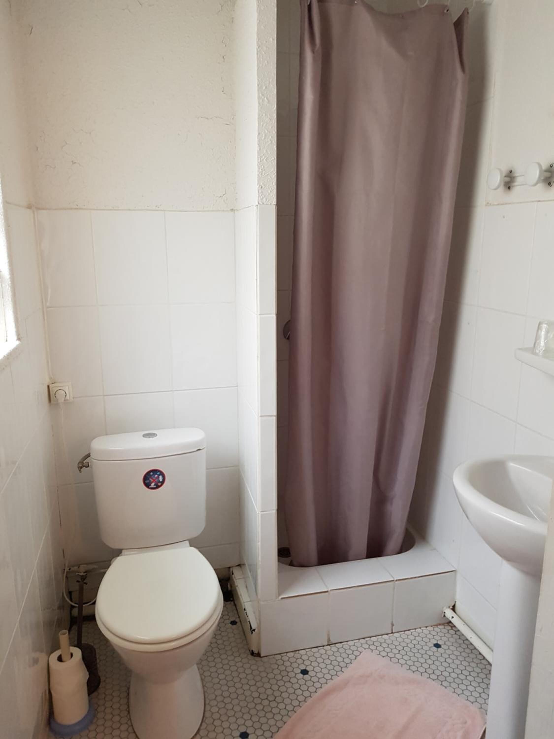 Ein kleines Badezimmer mit Toilette, Duschvorhang, Waschbecken und WC-Bürste.