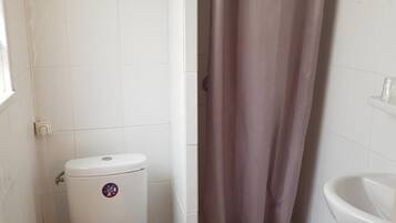 Ein kleines Badezimmer mit Toilette, Duschvorhang, Waschbecken und WC-Bürste.