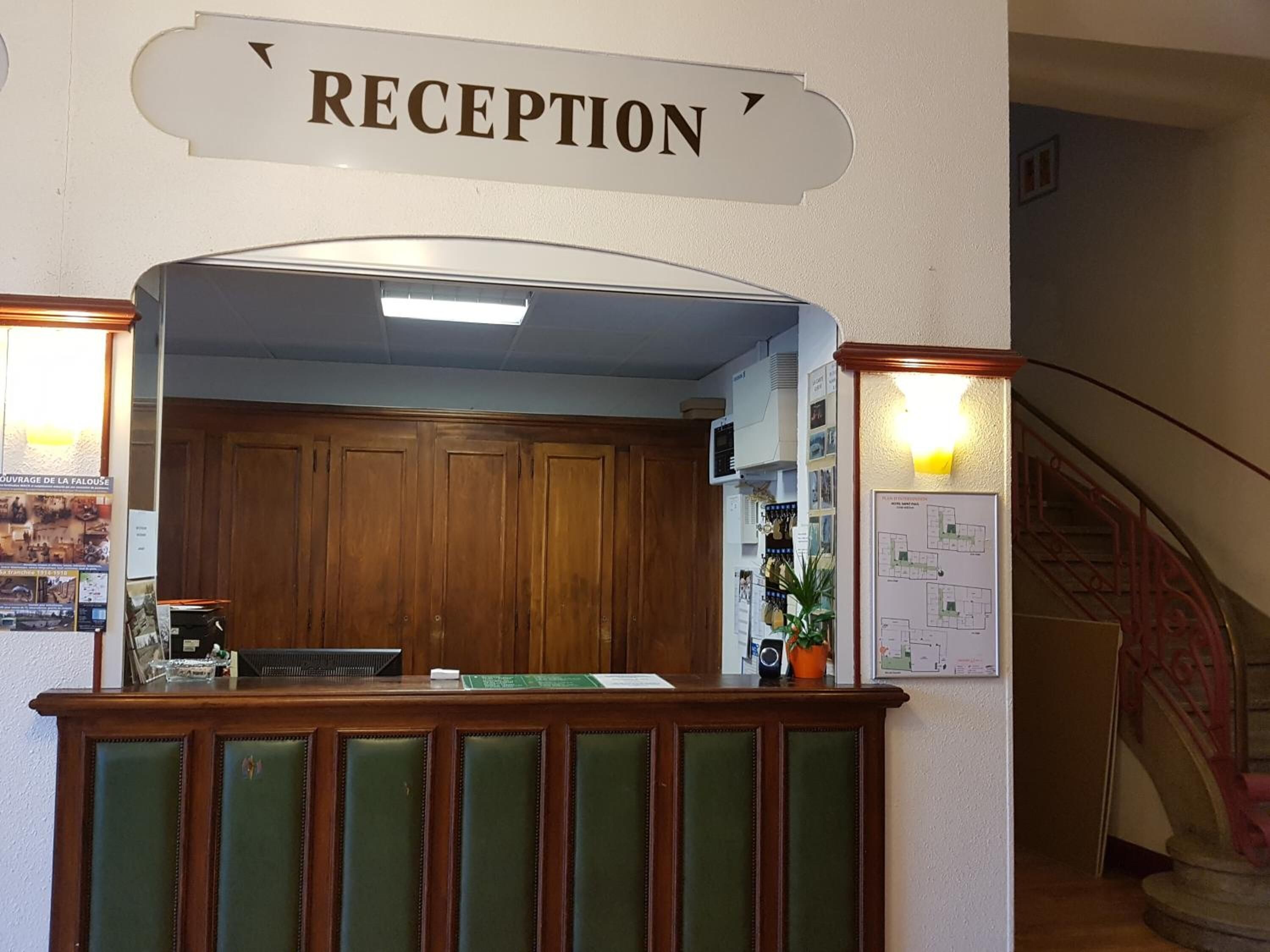 Un espace d’accueil avec un bureau en bois, des sièges rembourrés de couleur verte et un panneau indiquant « RÉCEPTION ».