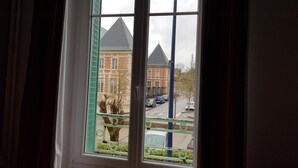 Una ventana con vistas a un edificio de techo puntiagudo y una calle con coches estacionados.