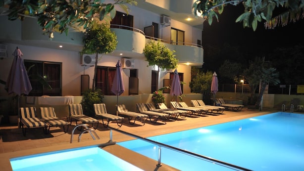 A swimming pool with lounge chairs and umbrellas, surrounded by a building with balconies and air conditioning units. - Anseli Hotel (Rhodes)