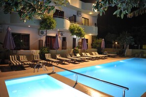 A swimming pool with lounge chairs and umbrellas, surrounded by a building with balconies and air conditioning units. - Anseli Hotel (Rhodes)