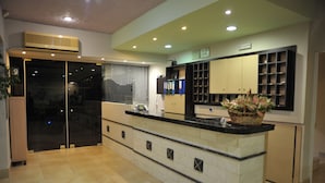 A modern kitchen with a central island, built-in cabinets, and a large window with blinds. - Anseli Hotel (Rhodes)