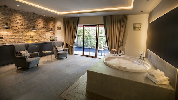 A modern bathroom with a large bathtub, a seating area with a sofa and armchairs, and a view of the outdoors through a sliding glass door. - Cityloft 24 (Istanbul)