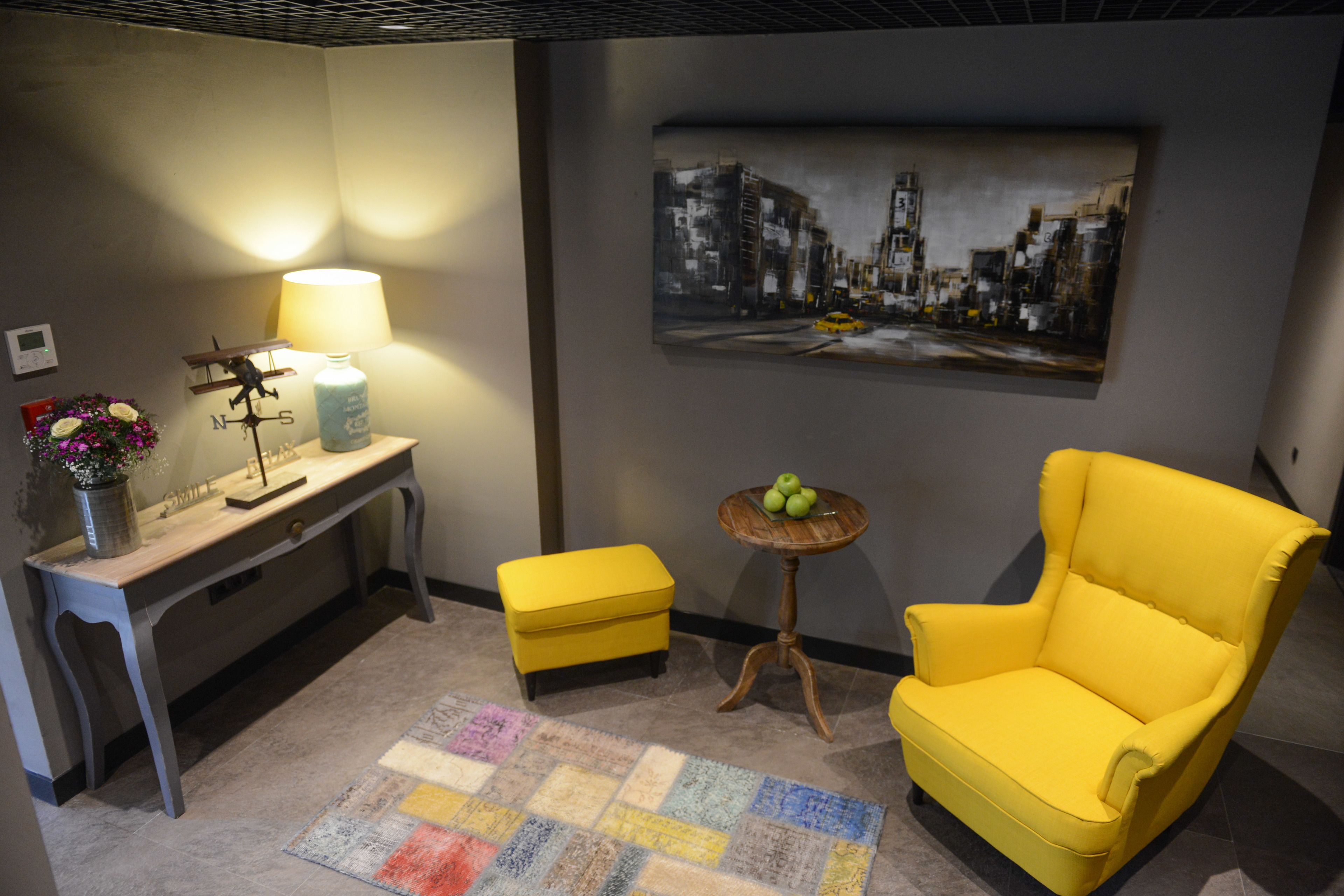 A room with a desk, a yellow armchair, a small round table with apples, a lamp, and a painting on the wall.