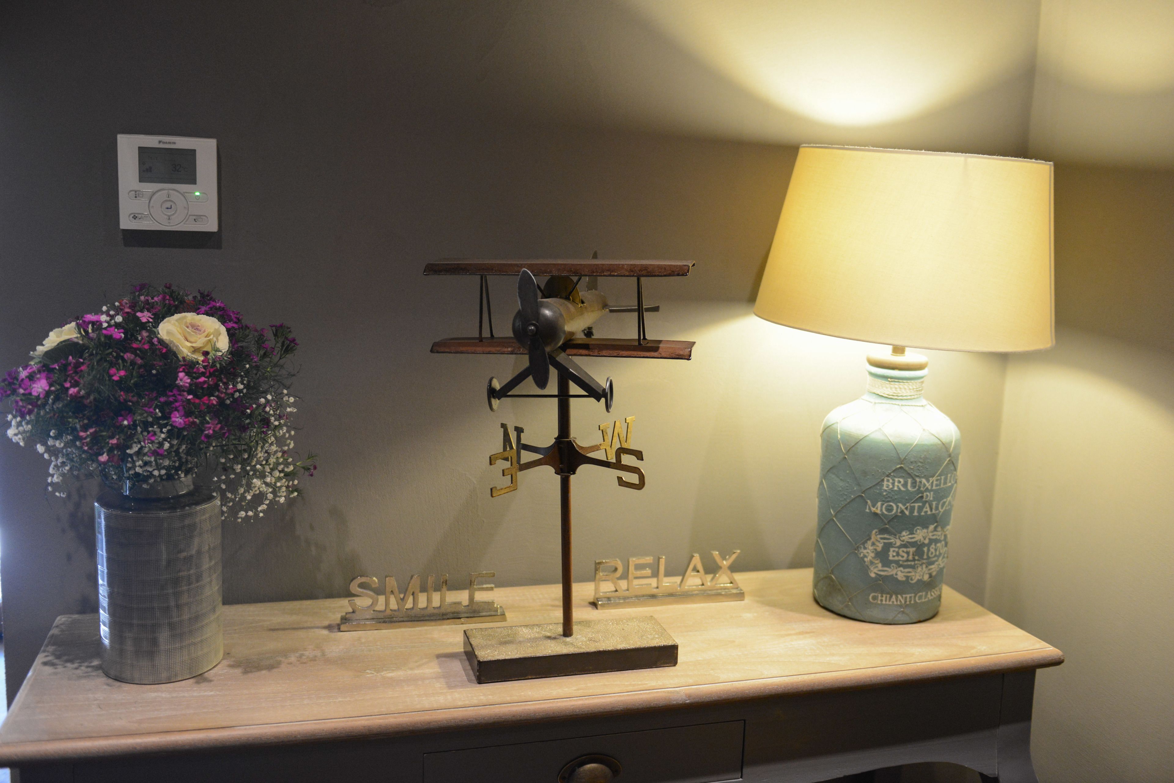 Une table en bois, sur laquelle se trouvent un petit modèle d’avion, un vase avec des fleurs et une lampe.