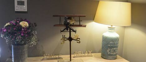 Une table en bois, sur laquelle se trouvent un petit modèle d’avion, un vase avec des fleurs et une lampe.