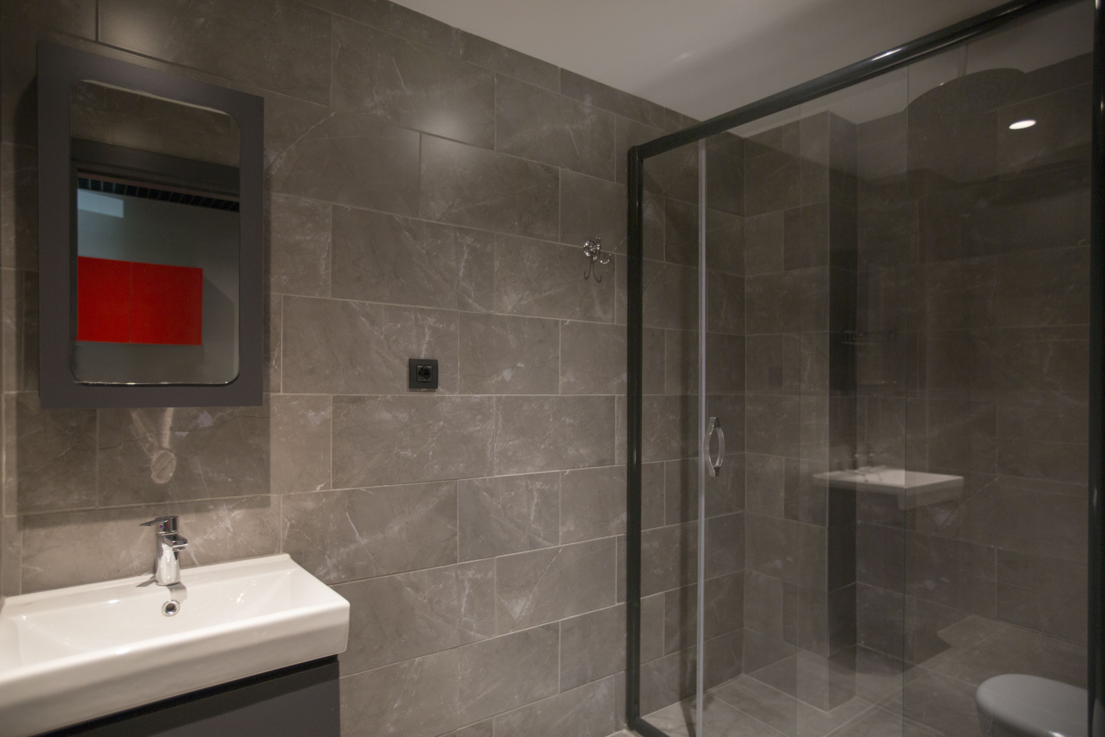 A modern bathroom with a glass-enclosed shower, a white sink, and a mirror with a red accent.