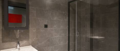 A modern bathroom with a glass-enclosed shower, a white sink, and a mirror with a red accent.