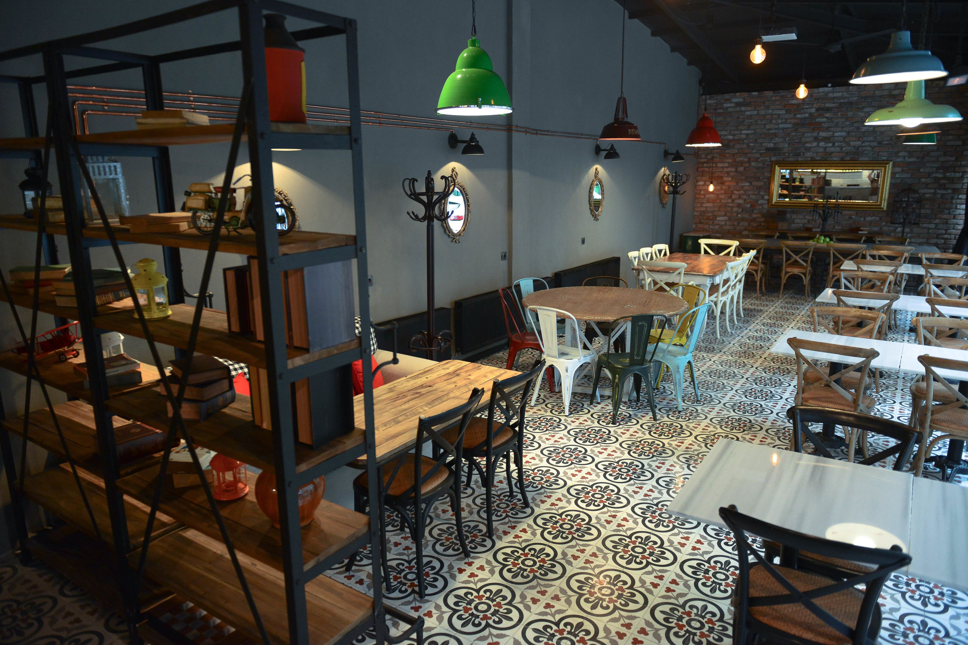 A restaurant with wooden tables and chairs, a patterned floor, and hanging green and red pendant lights.