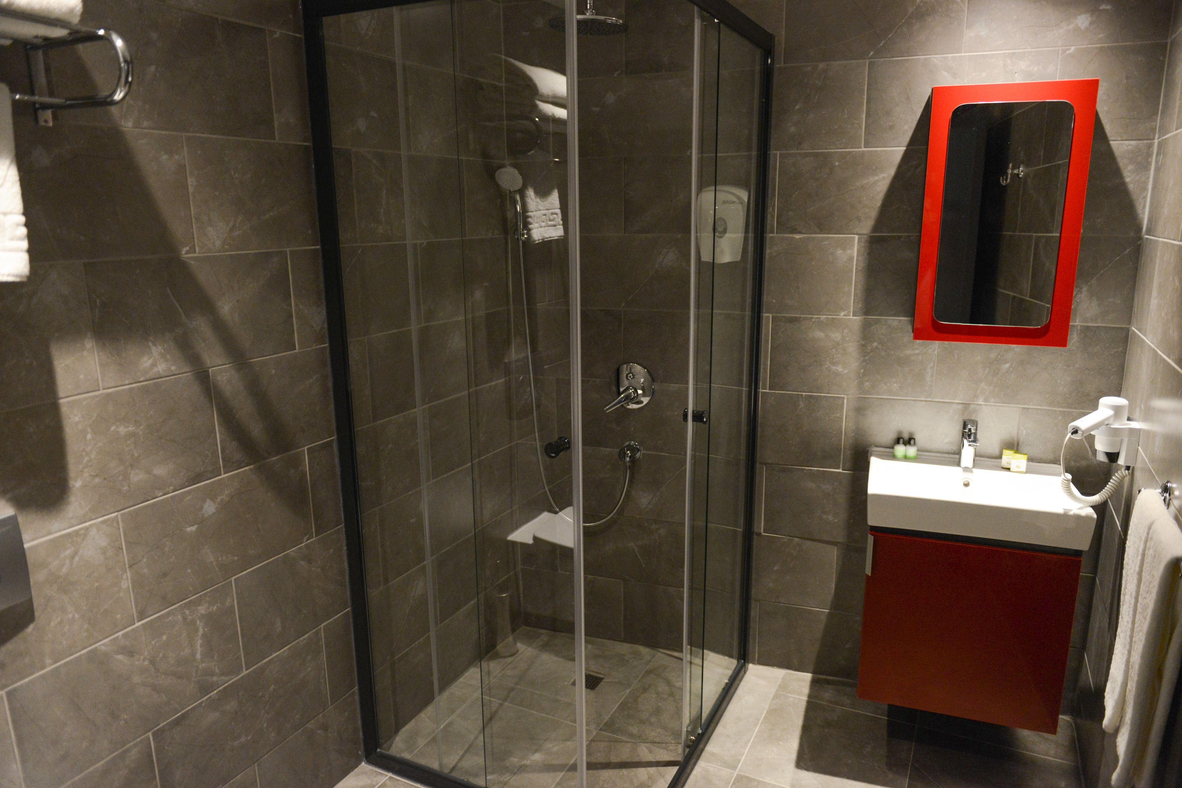 A modern bathroom with a glass-enclosed shower, a red-framed mirror, and a white sink with a red cabinet.