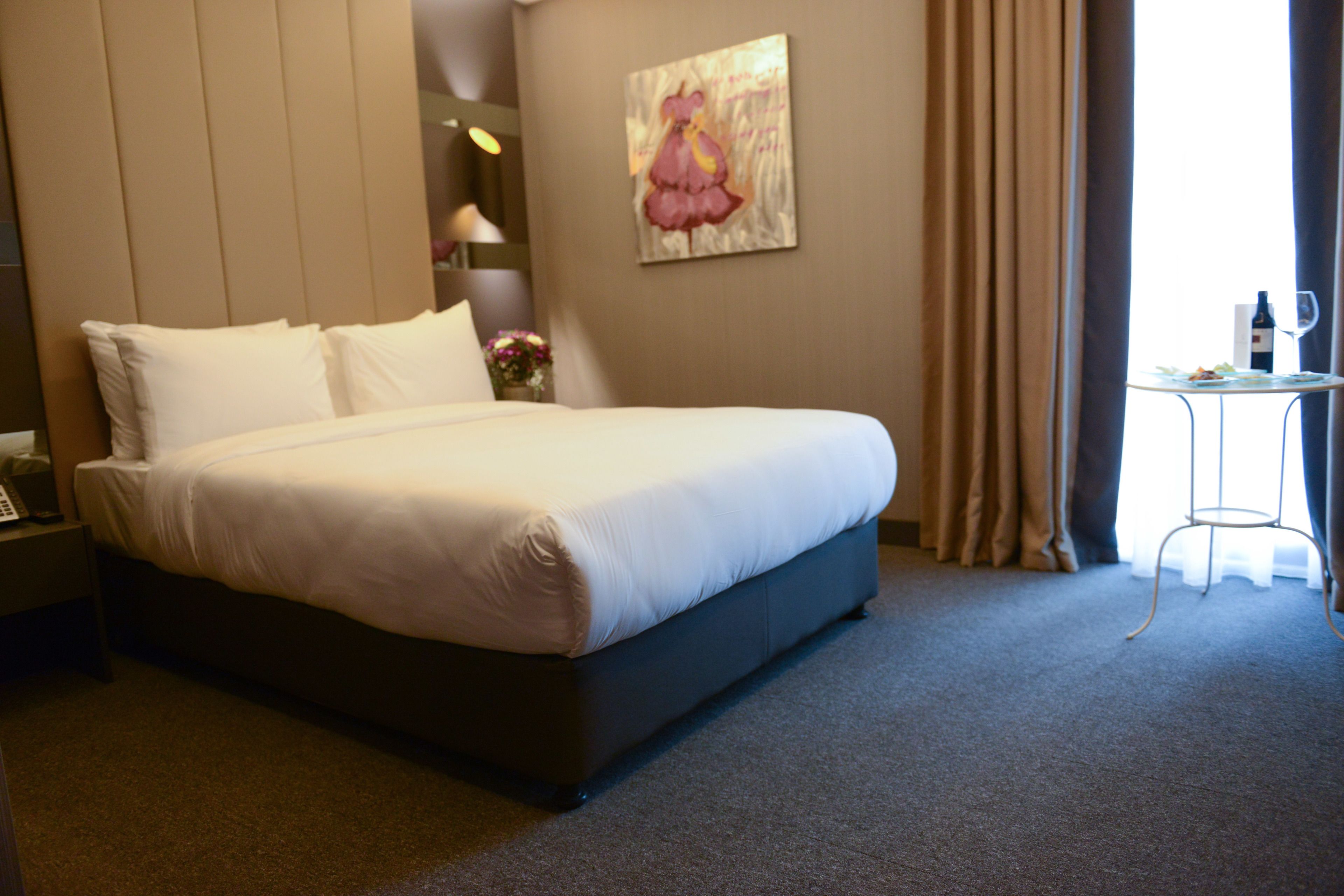 Une chambre d’hôtel avec un grand lit, une table de chevet, une lampe, un tableau au mur et une fenêtre avec des rideaux.